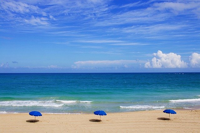 Piesková pláž s troma modrými slnečníkmi.jpg