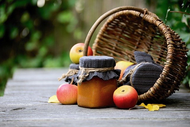 Prútený košík s jablkami a zaváraninami na drevenom stole